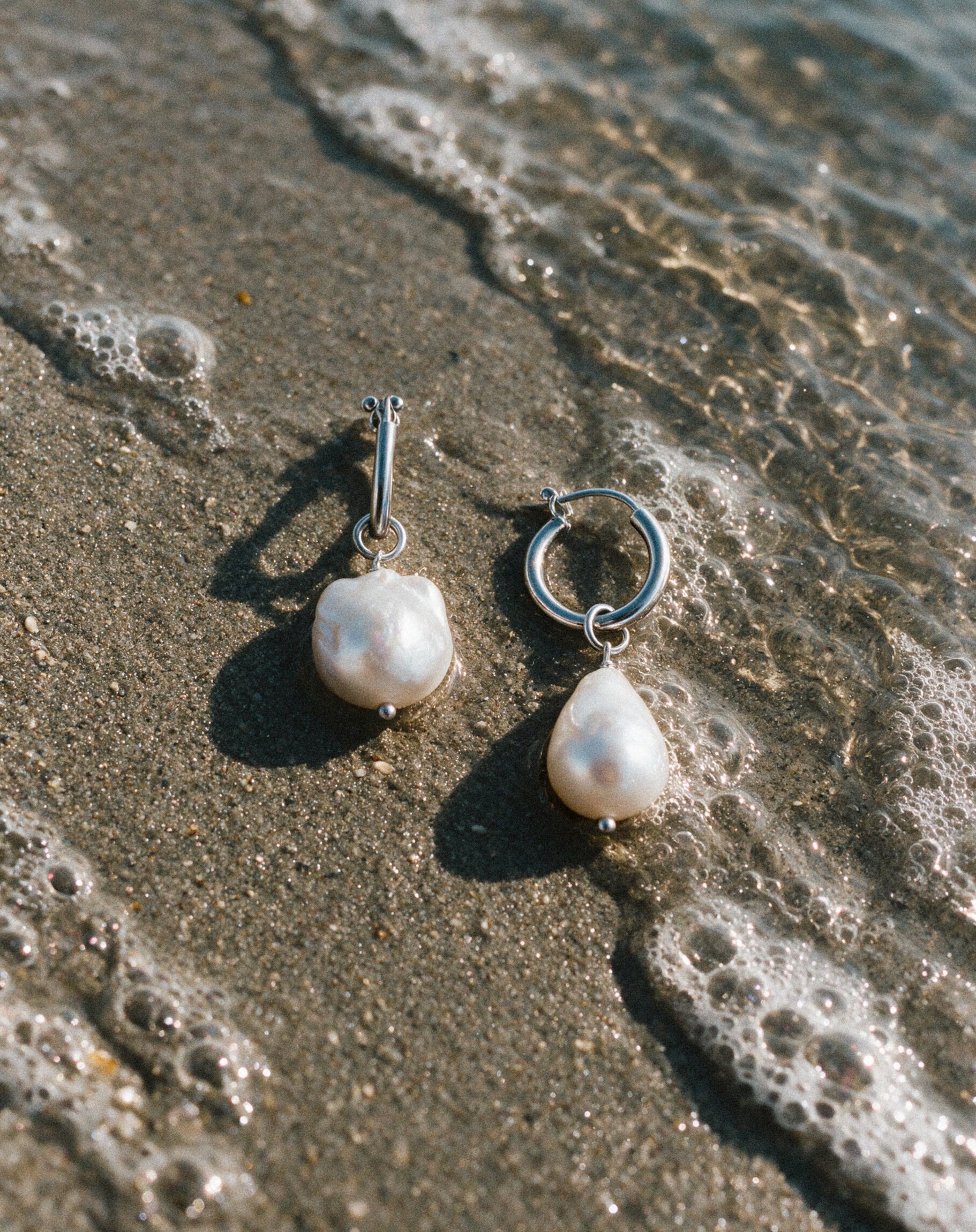 Close-up Pearl Naked Mermaid Tear Earrings on the sand.
