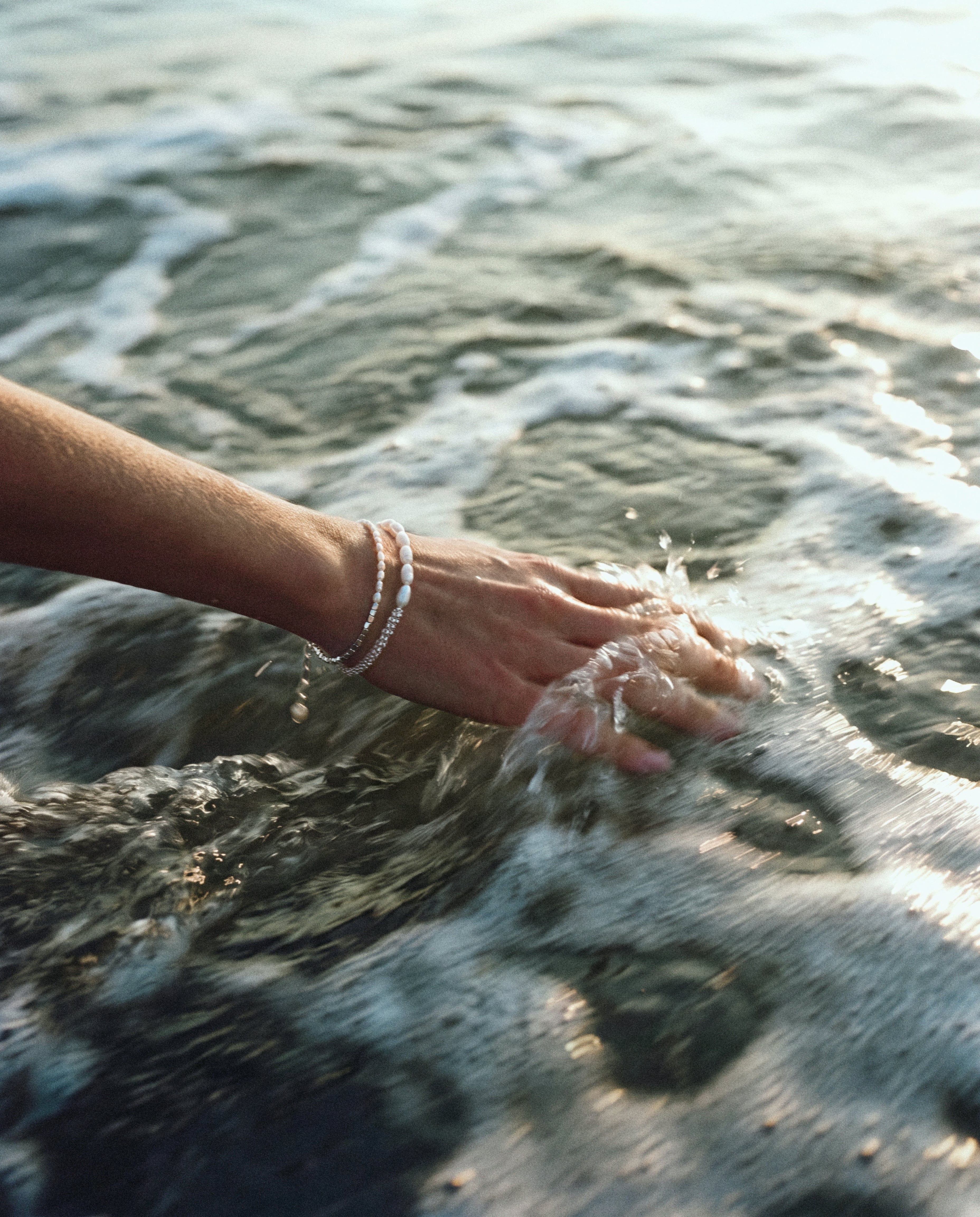 Close-up of arm in water wearing Pearl Naked Midtide and Calypso Bracelet in silver.