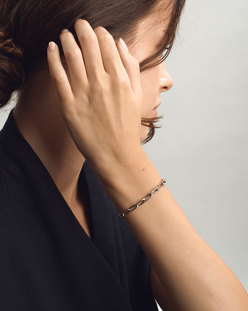 Female model wearing SEASTER Swell Bracelet in Silver, hand lifted to her hair to show the silver chain links at her wrist in profile, for COLD SKIN.