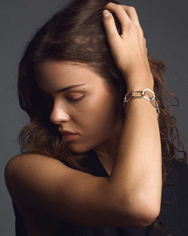 Female model wearing STRUGA Blade Medium Links V.2 Bracelet in Silver, portrait with hand raised to her hair showing the square silver links on the wrist, for COLD SKIN.