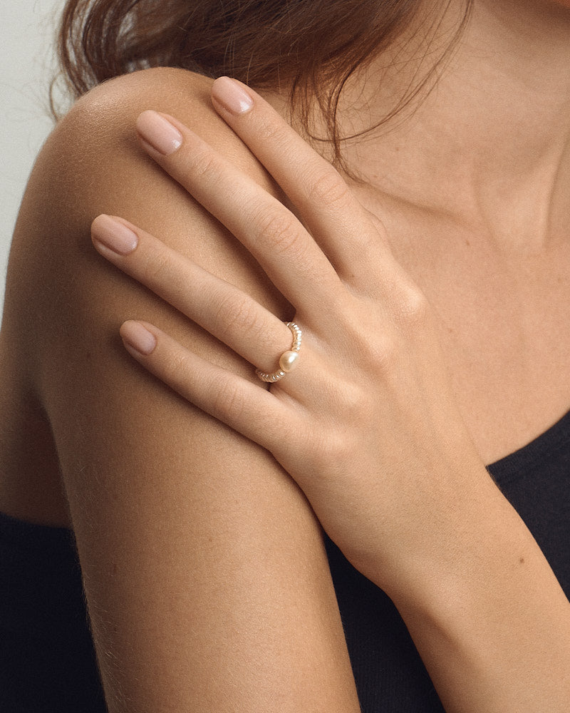 Female model wearing PEARL NAKED Bubble Ring in Pearls, gold-toned beaded band with a central pearl, hand resting on her bare shoulder, for COLD SKIN.