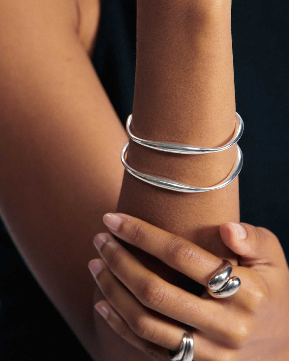 Female model wearing BAIXA Vicky Bracelet in Silver, smooth silver bangles on her forearm, with silver rings also visible on her fingers, for COLD SKIN.