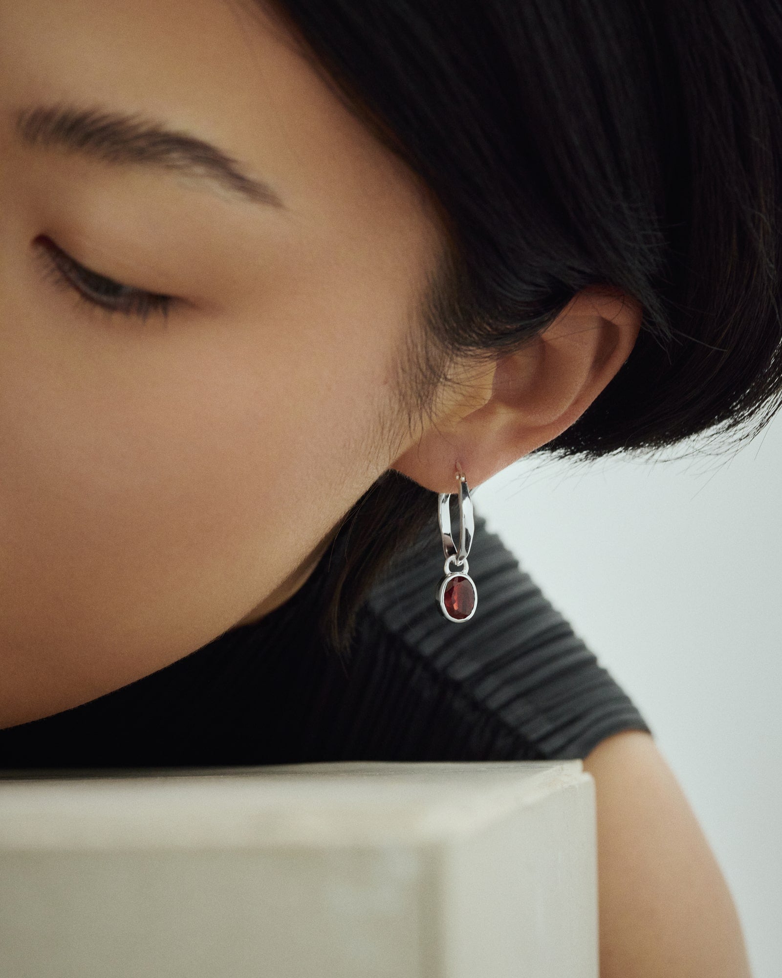 Weibliches Model trägt Arishi Ideal Hoops in Silber mit Granatstein.