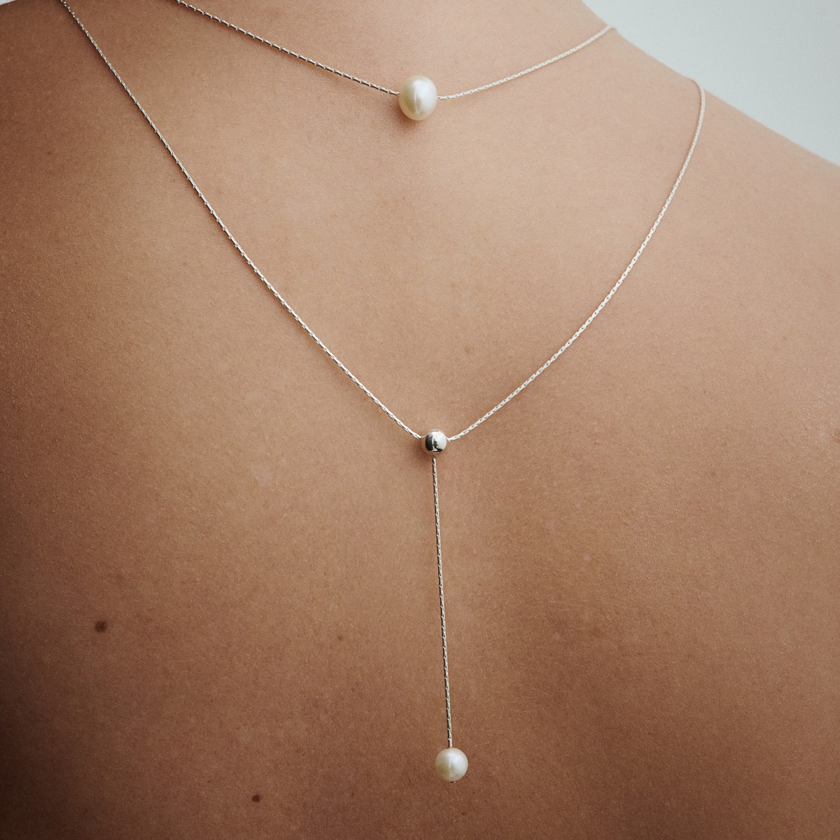 Female model wearing the Pearl Naked Double Chain Necklace with pearls for COLD SKIN.