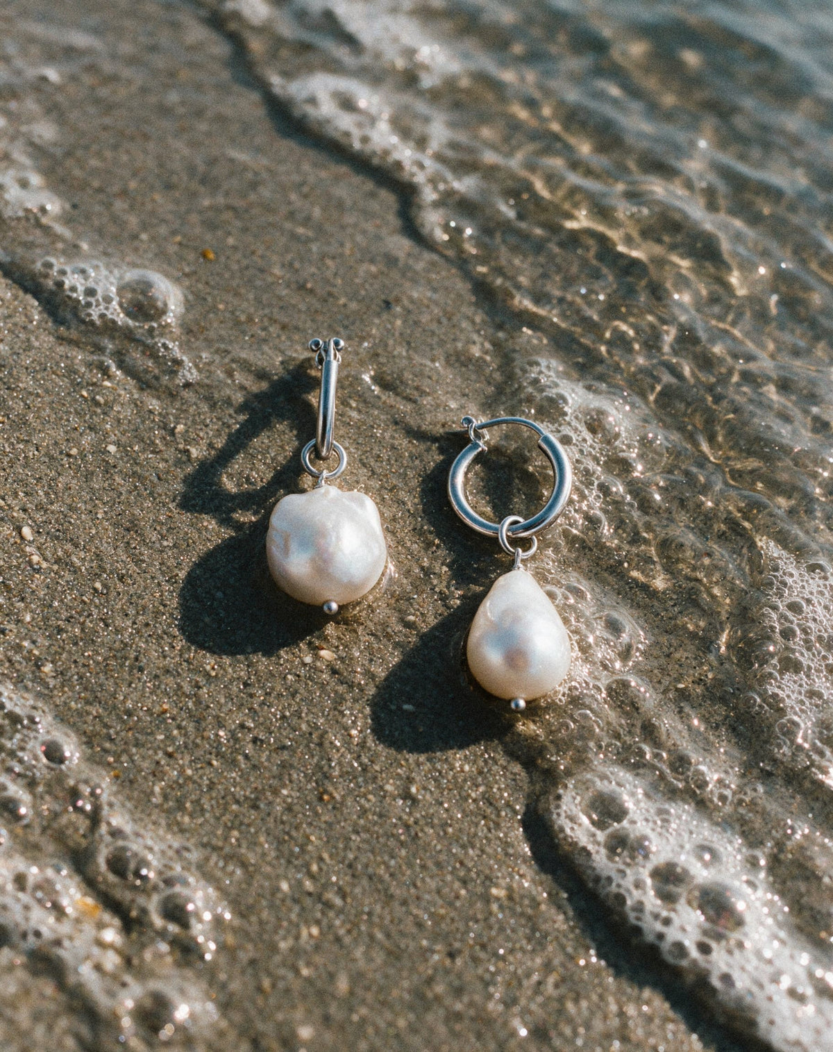 Close-up Pearl Naked Mermaid Tear Earrings on the sand.