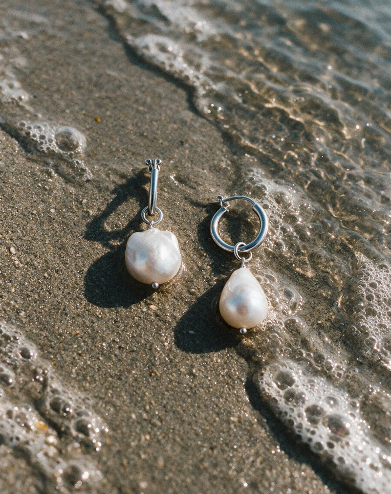 Close-up Pearl Naked Mermaid Tear Earrings on the sand.