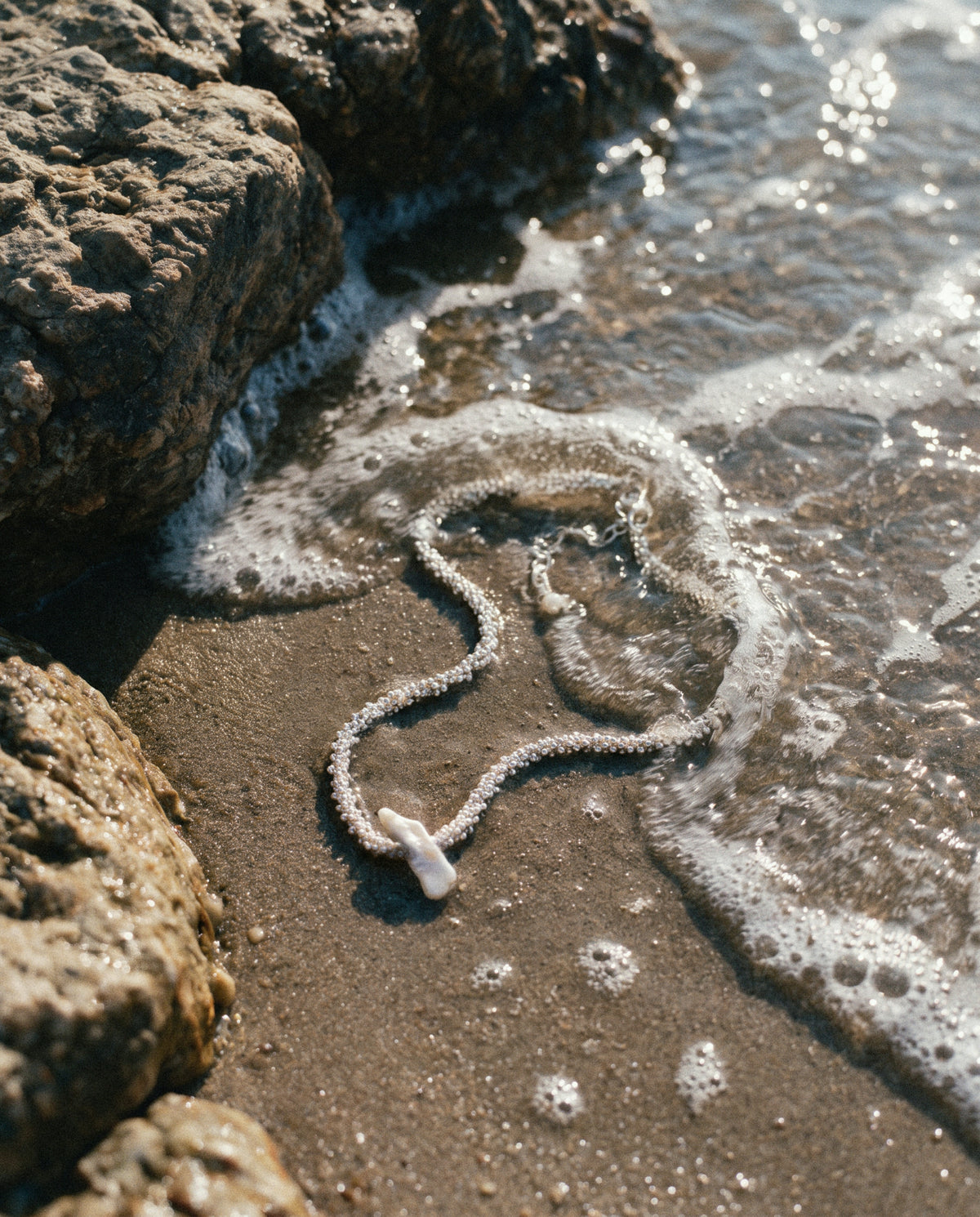 Close-up of the Pearl Naked Reef Pearl Choker in silver between rocks and waves.