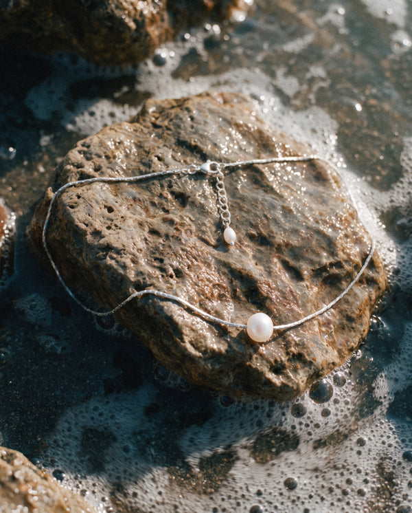 Close-up of Pearl Naked Sunny Dust Necklace in silver on a stone.